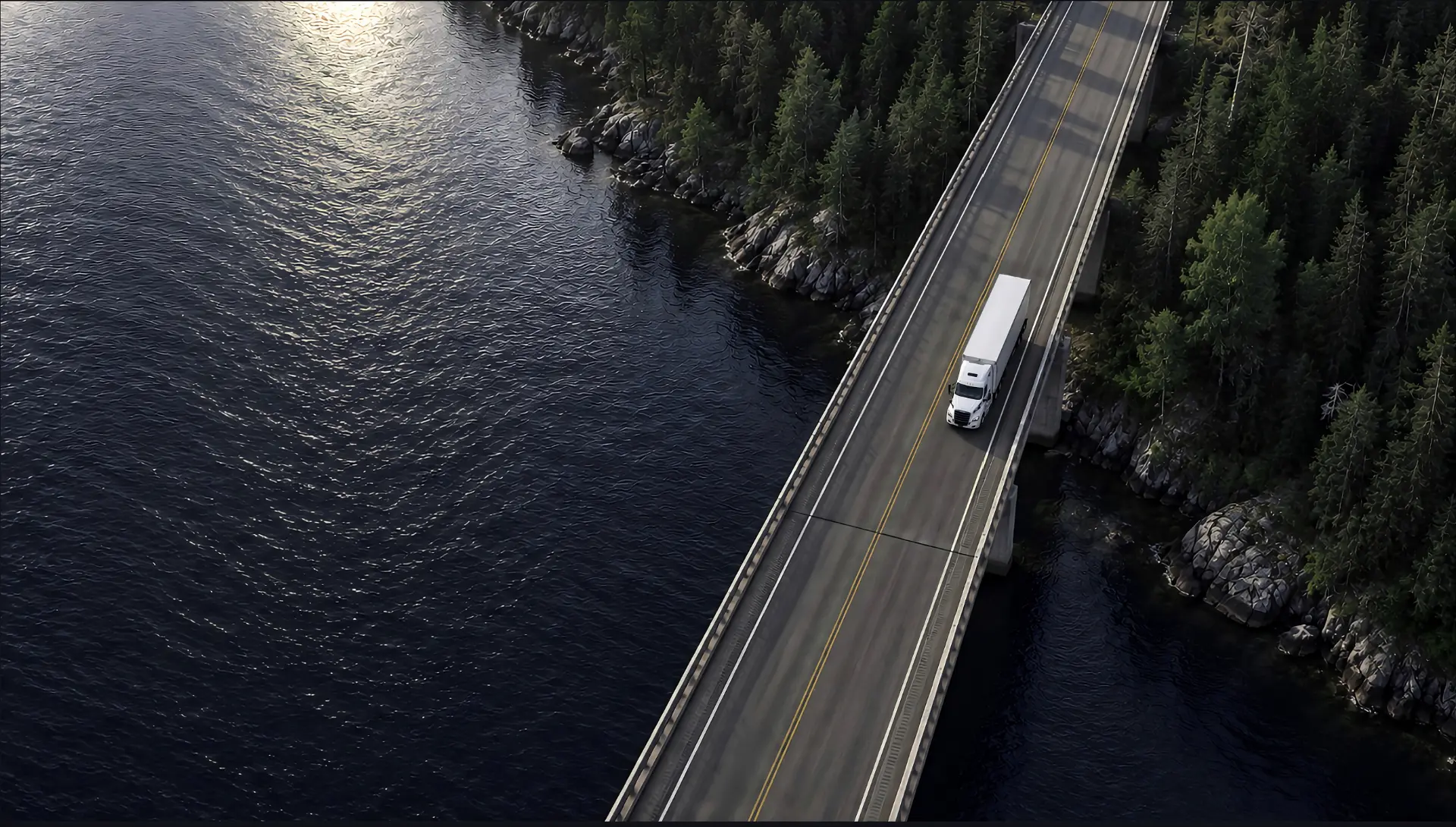 A dry van semi truck crossing a bridge over water